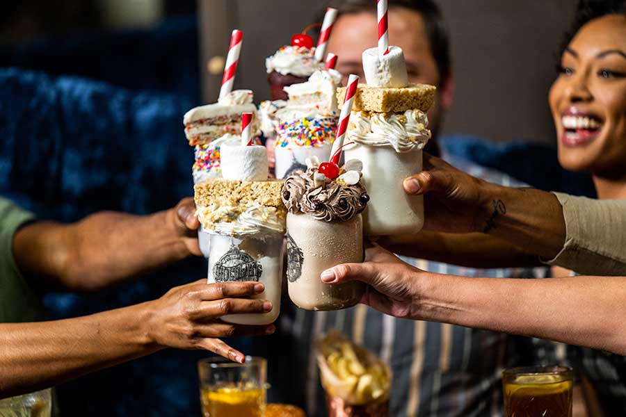 Assorted milkshakes topped with whipped cream and desserts, held by a group of people at a restaurant table.